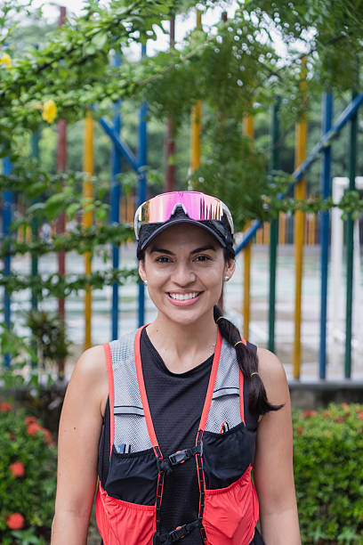 Woman trail runner smiling at camera, wearing a hydration vest and cap with mirrored sunglasses
