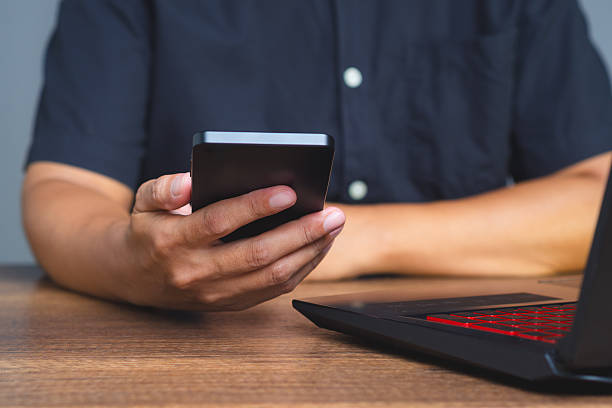 istock Hand holding smartphone next to laptop on desk. 2239856510