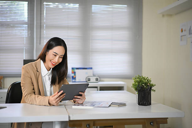 istock Confident businesswoman sitting at desk using digital tablet, smiling while working in modern office 2239857985