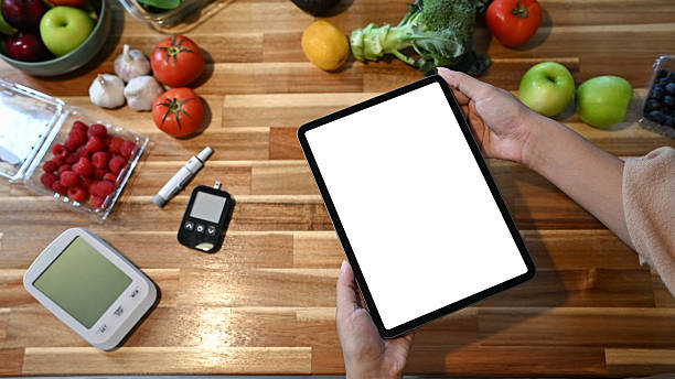 Hands holding digital tablet with blank white screen surrounded by fruits, vegetables, and health monitoring devices