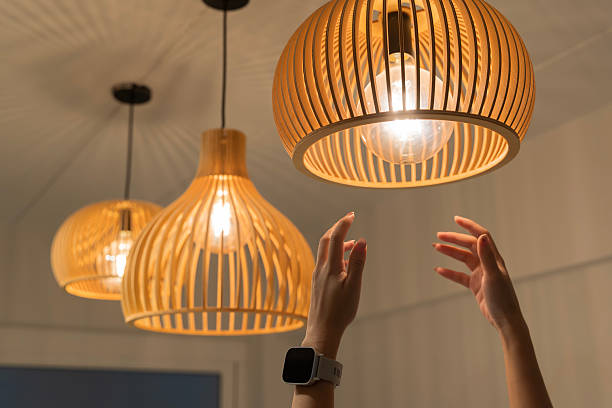 istock Hand reaching to adjust modern wooden pendant ceiling lamp with glowing light bulb interior home decoration 2239863994