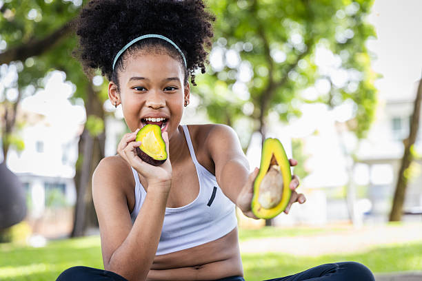 Girl athlete eating avocado in park enjoying healthy snack and active lifestyle