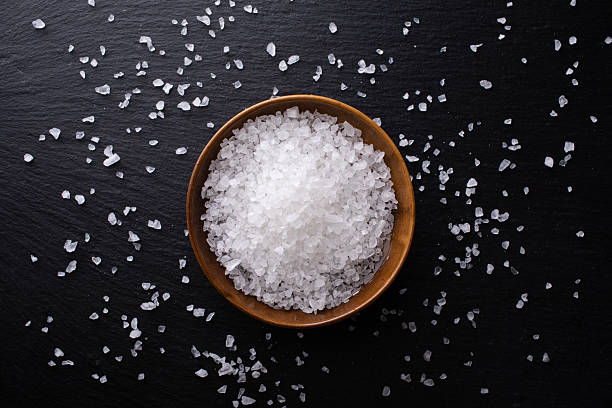 istock Pile of sea salt in ceramic bowl on black stone kitchen table top view. 2239868744