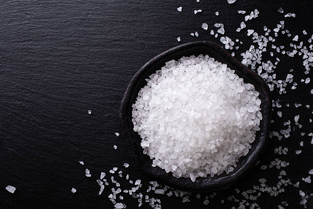 istock Pile of sea salt in ceramic bowl on black stone kitchen table top view. 2239868769