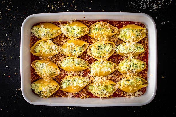 Ready to cook pasta conchiglie stuffed with cheese and spinach with tomato sauce in baking dish on black table