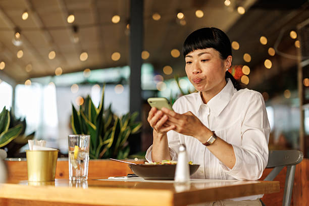 istock Beautiful Asian businesswoman using smart phone while having lunch in bright, cozy restaurant 2239873621