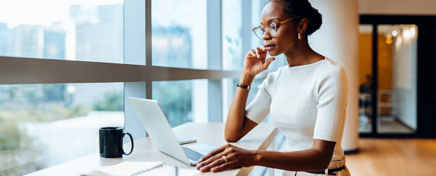 istock Woman using laptop and thinking while working near large window 2239880229