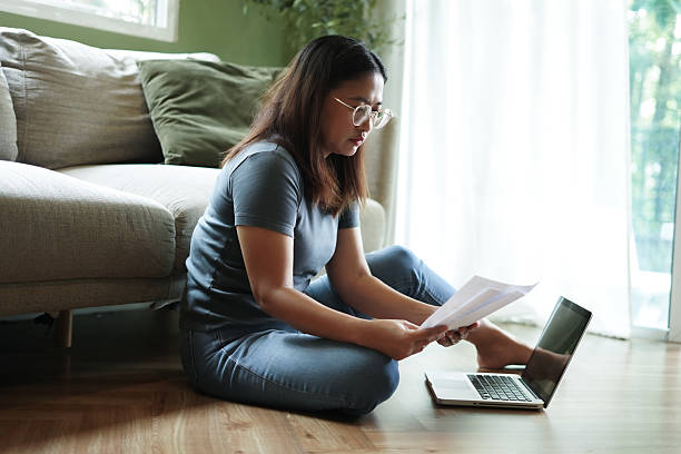istock Woman sits checking financial papers in front of a sofa. 2239880270