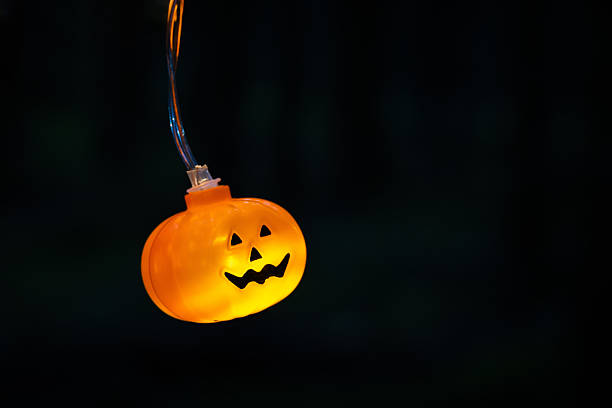 Illuminated plastic pumpkin face lights hanging on branch creating festive spooky atmosphere perfect for Halloween party and seasonal home decor