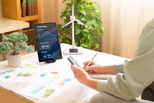 istock Person studying wind energy performance data on a tablet with a miniature wind turbine model and charts on the desk, highlighting sustainable energy management and ecological future planning 2239883948