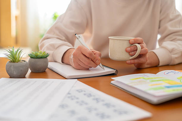 istock Woman writing notes in a spiral notebook while holding a coffee cup at a wooden desk with planner, documents and succulents  focused, organized home office routine 2239884161