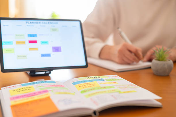 istock Person organizing daily tasks and appointments for work and home responsibilities using a physical planner and a digital calendar on a tablet for an organized lifestyle 2239884170