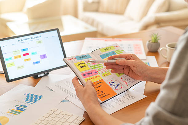 istock Person's hands holding an open paper planner, writing down notes, and managing appointments while sitting at a desk with a digital calendar and printed charts 2239884248