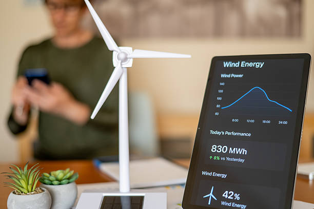 istock Person in blurred background using smartphone while tablet in foreground shows wind energy monitoring dashboard beside wind turbine model and potted plants, eco tech concept 2239884399