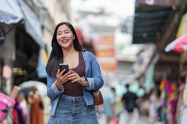 istock Asian woman smiling using phone navigating city market 2239885546