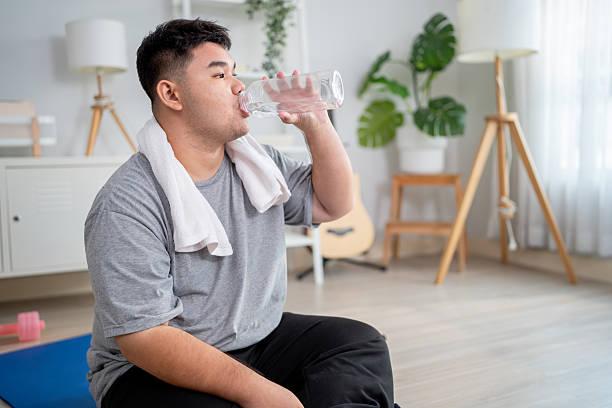 istock Exhausted Asian plus-size man taking a break while workout in house. Attractive curvy male spend time drinking bottle of water after exercise to improve health and lose weights in living room at home. 2239887186