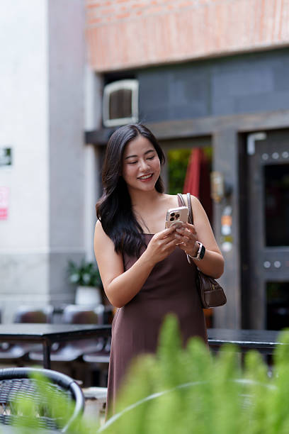 Young asian woman smiling using smartphone outdoors