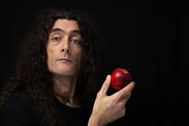 Portrait of a Man Holding a Red Apple in Shadow. Dramatic portrait of a man featuring a low-key lighting style that contrasts a well-lit face and hand against a predominantly black background.