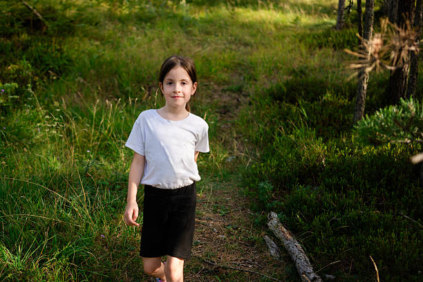 Young girl walking along a woodland trail on a bright summer day, surrounded by lush green grass and trees