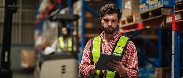 istock Warehouse workers and manager in reflective vests inspecting inventory, using digital tablet for stock control, logistics, supply chain management, and modern industrial warehouse operations. 2239894922