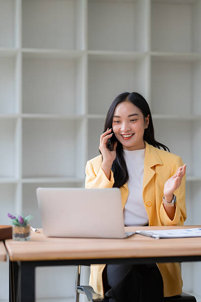 Asian businesswoman talking on cell phone while working on laptop