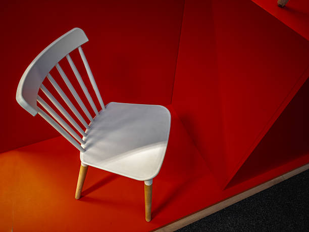Minimalist composition with a white chair and wooden legs placed against a bold red background. Contemporary interior design concept emphasizing color contrast and simplicity.