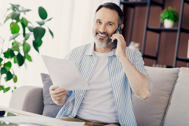 istock Professional man talking on phone while reviewing documents, in a contemporary home interior with natural light 2239898358