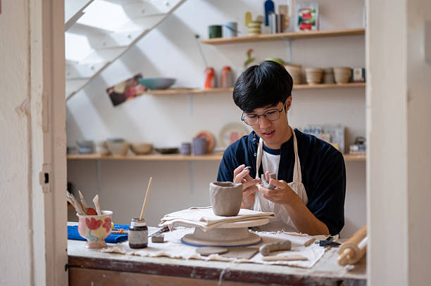 istock Pottery artist holding brush adding clay slip to glue mug handle at working table in class or studio 2239899571