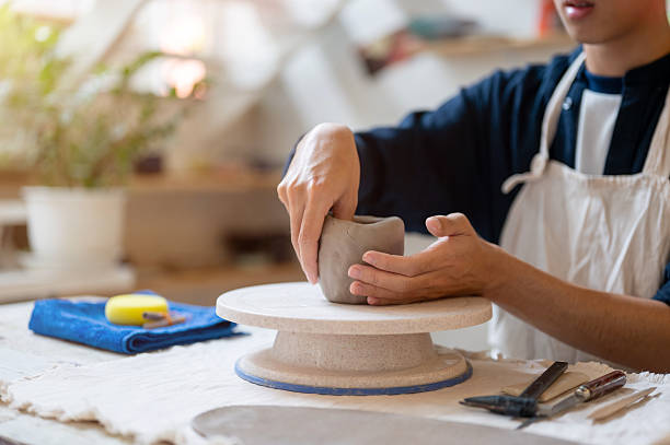istock Close up pottery artist molding a clay mug over throwing wheel at working table in class or studio. 2239899694
