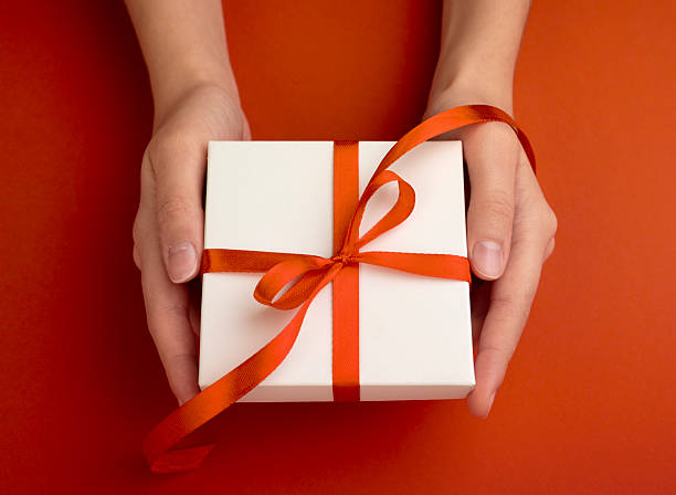 istock Hands holding white gift box decorated with red ribbon top view closeup.Holiday present concept. 2239901768