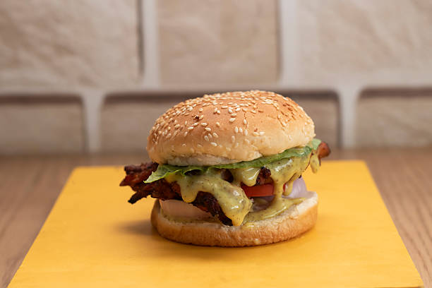 istock Classic Chicken Burger on Yellow Board include lettuce, sliced tomato, onion, creamy green sauce, and Sesame Bun on blurred brick wall background side view 2239902130