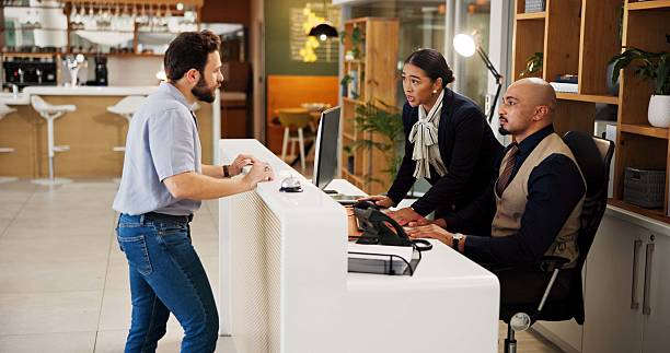 istock Man, welcome and help desk at hotel with check in, talk and booking info for suite on vacation. People, concierge and client at counter for reservation, discussion and hospitality service at lodge 2239904167