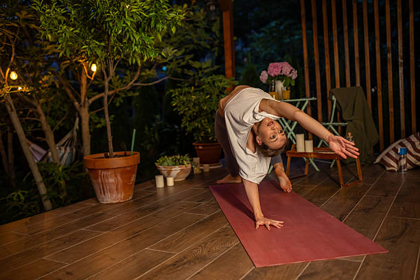 istock Woman Practicing Yoga Outdoors on Wooden Deck Surrounded by Plants and Lights 2239906297