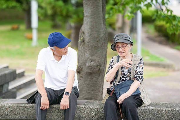 Two elderly people sitting on a stone wall, one wearing a blue hat. They are talking to each other