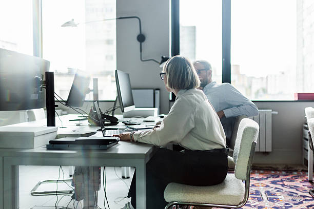 istock Two coworkers collaborate at a modern office desk with laptops, monitors, and documents 2239914250