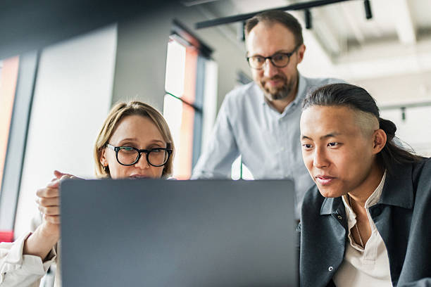 istock Three professionals collaborate in a modern office around a laptop, sharing ideas and focusing on work tasks 2239914372
