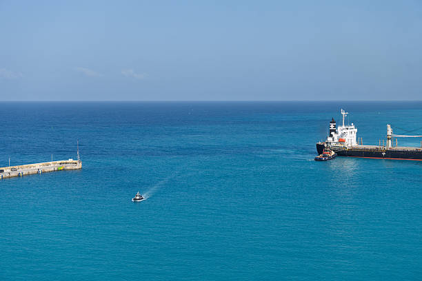 Bridge Town, Barbados - Feb 2024Cargo ship docked at harbour pier with small motorboat navigating turquoise sea under clear blue sky