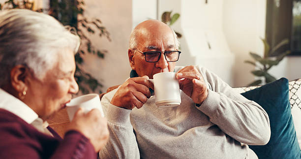 istock Coffee, drinking and senior couple on sofa in home with conversation, bonding or relaxing together. Happy, tea and elderly man with woman for retirement in living room for calm morning in house. 2239920131