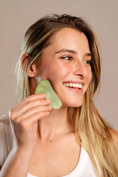 istock Woman using gua sha jade tool on cheek, massaging face for beauty and skincare routine, smiling for self-care 2239920455