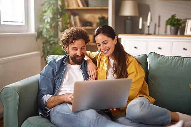 istock Happy couple relaxing on sofa, browsing internet on laptop at home 2239921541