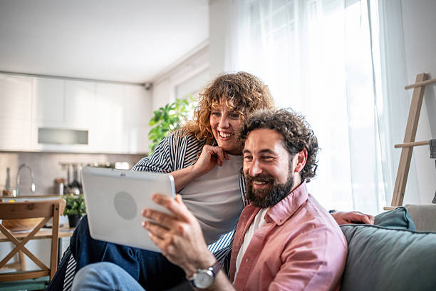istock Couple relaxing on sofa at home browsing tablet 2239922461