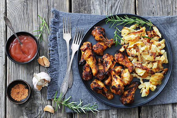bbq chicken wings with fried potatoes on a plate with rosemary on rustic grey wood table with forks and ketchup, horizontal view from above, flat lay, not AI generated