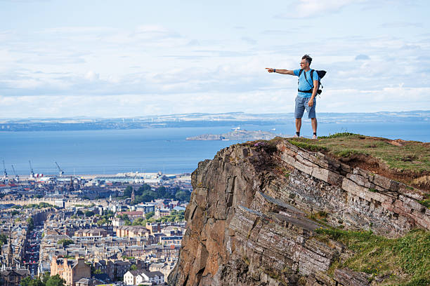 istock Hiker points from high cliff, viewing cityscape and ocean scene 2239925289
