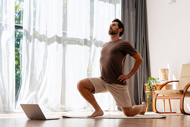 istock Handsome, bearded Hispanic man practicing yoga stretch indoors with laptop guidance 2239926011