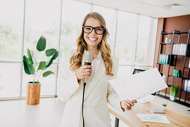 istock Confident young businesswoman holding a microphone and documents in a modern office setting, exuding professionalism 2239936951