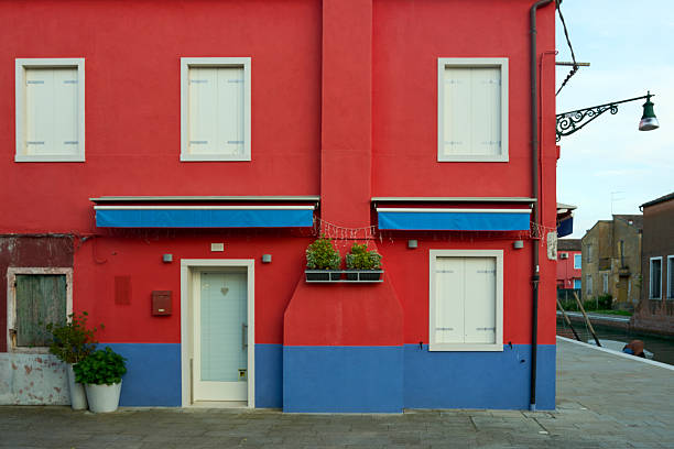 Colorful facade of a red and blue building with white shutters in Burano, Italy, showcasing vibrant architecture.
