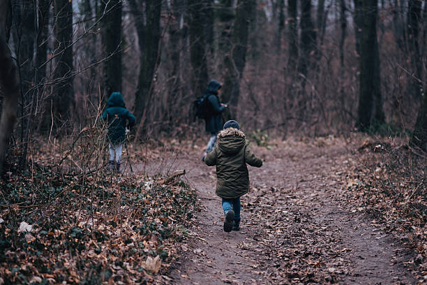 Children and adult walking on a natural path covered with dry leaves, enjoying nature and outdoor activity together