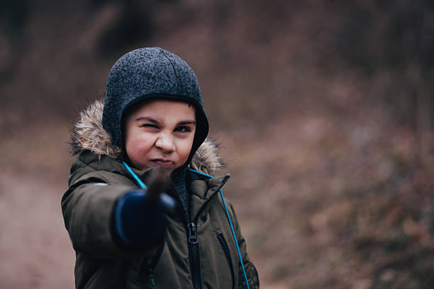 Young boy in winter jacket winking and pointing a finger directly at the viewer, showing playful, mischievous, confident attitude