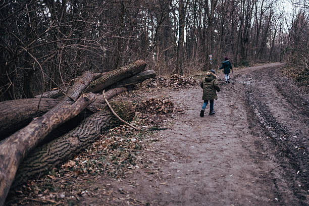 Two boys exploring natural forest path with fallen logs, enjoying a winter hike, promoting outdoor activity and adventure