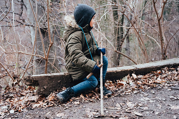 Young boy sitting outdoors on a log in a bare winter forest, holding a stick and observing the serene nature